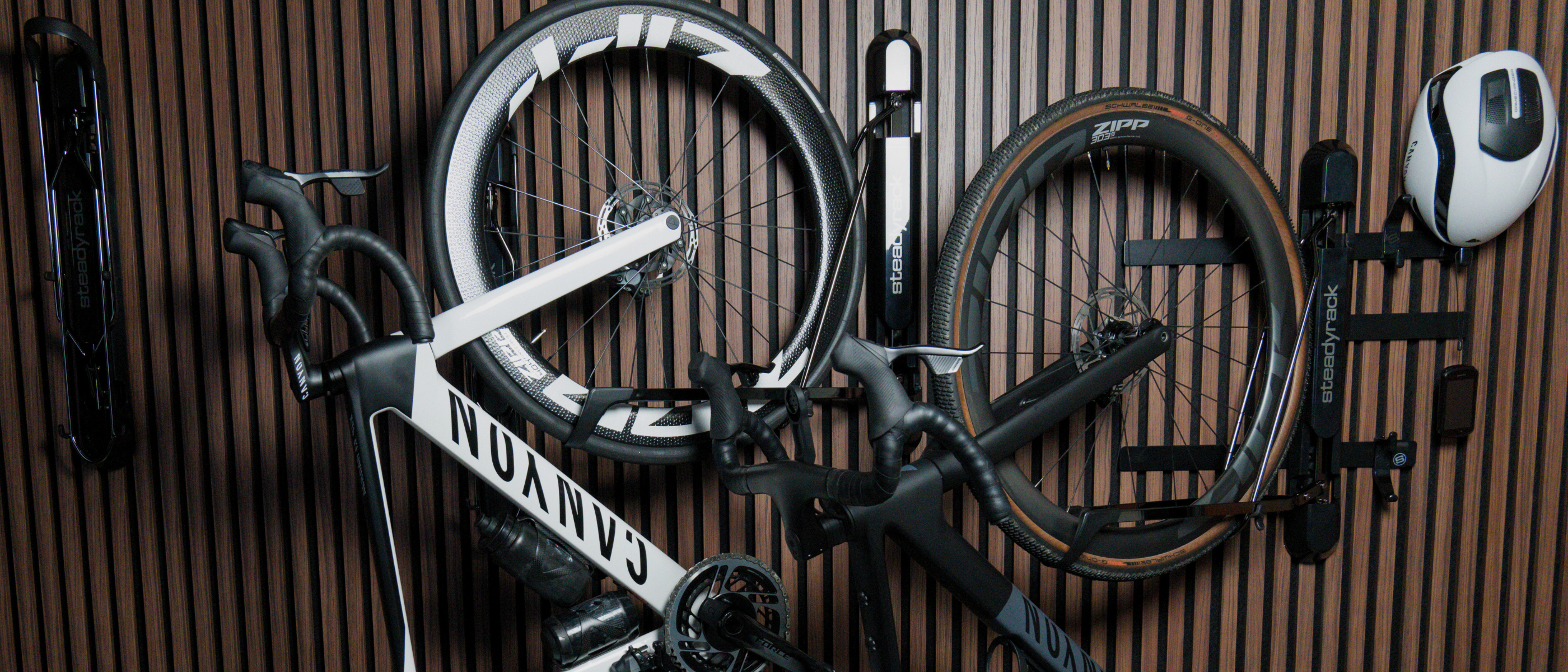 Two road style bikes hanging in wall mounted racks with gear holders on a wood look background. 