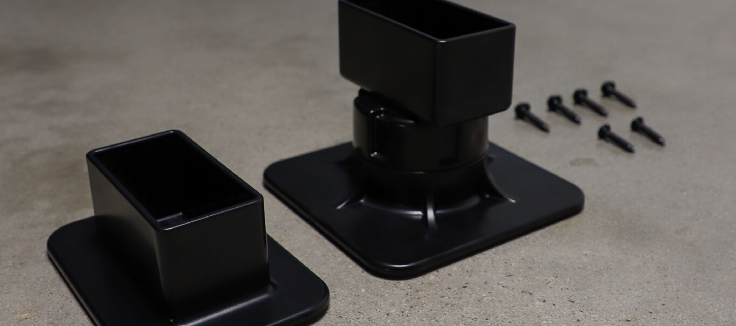 Black metal brackets with screws on a concrete surface