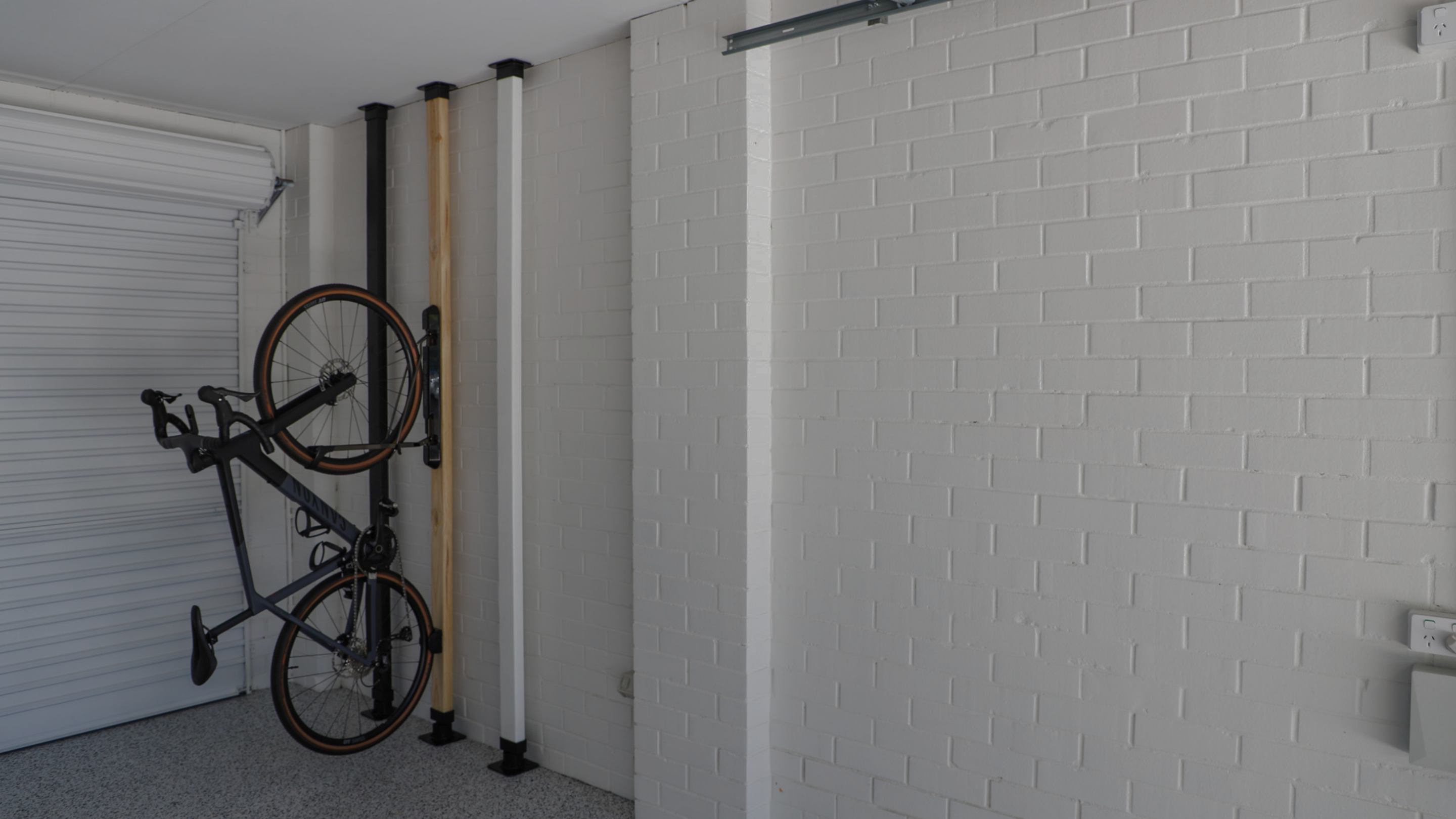 Bicycle mounted on a wall rack in a garage with white bricked walls.