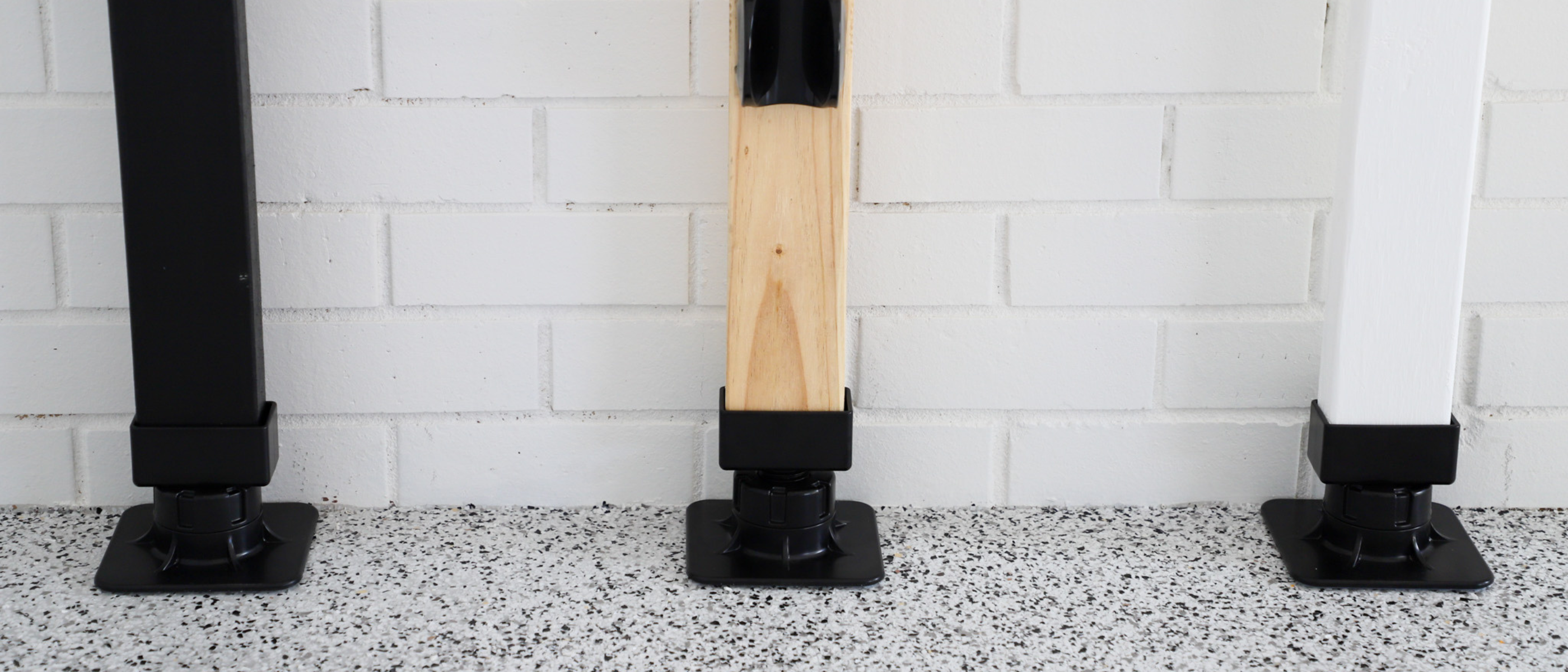 Three black bases with wooden poles against a white tiled wall.