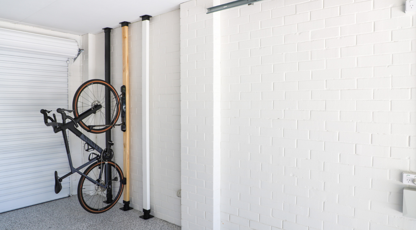 Bicycle mounted on a wall rack in a garage with white bricked walls.
